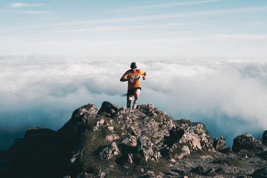 Man running on rocky mountain peak above clouds